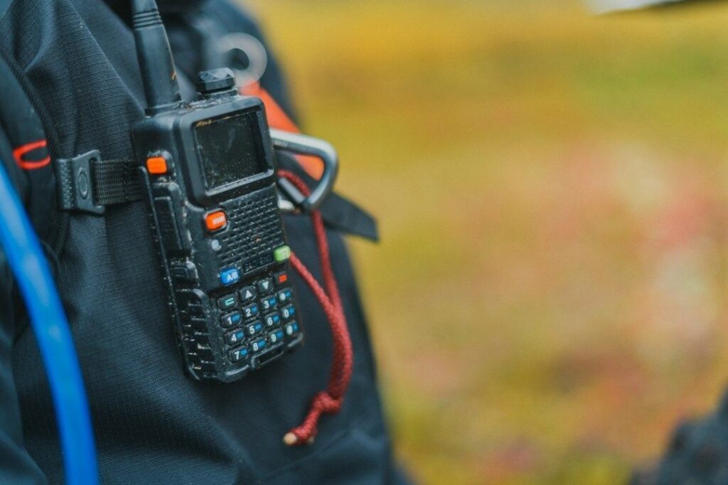 Handheld two-way radio clipped to a black outdoor backpack
