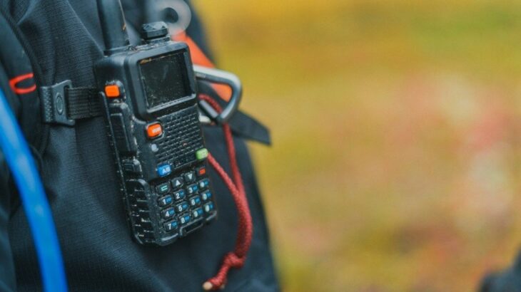 Handheld two-way radio clipped to a black outdoor backpack