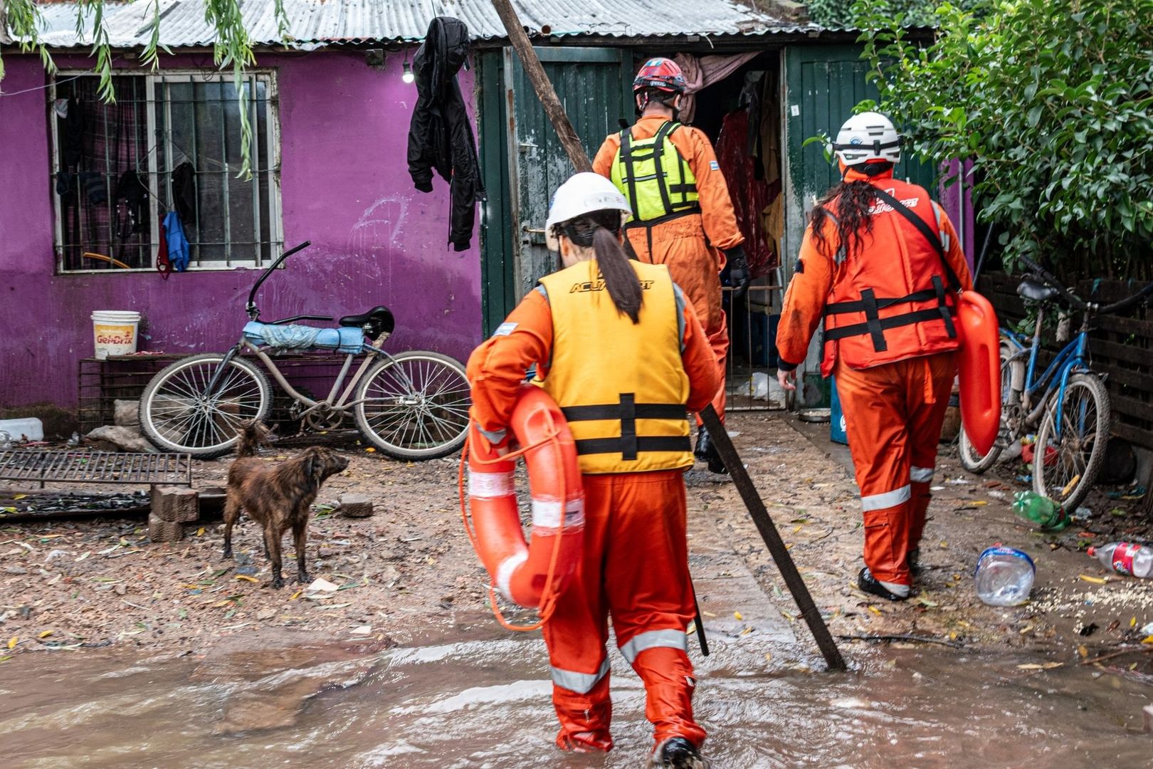 Rescue workers wade through floodwater outside a home
